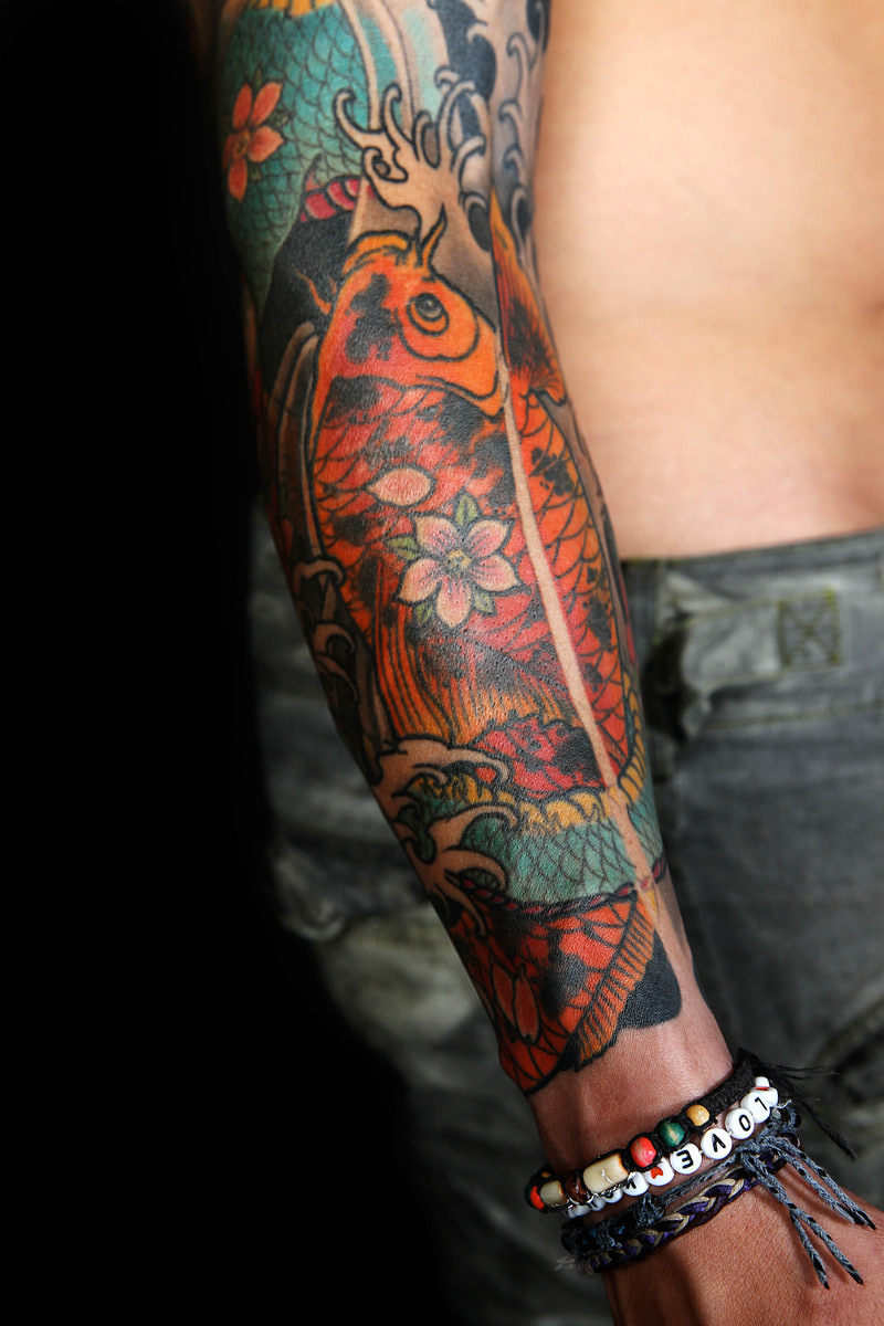 Orange koi forearm tattoo with cherry blossoms and waves